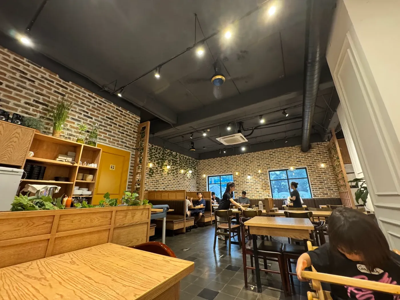 Không gian trong quán Gardenia: tường gạch mộc, bàn gỗ, ghế booth, cây xanh