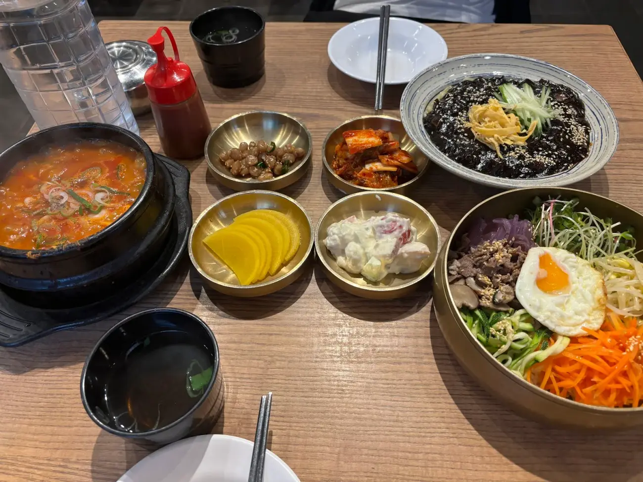 Mâm ăn Hàn nhìn từ trên: bibimbap, jjajangmyeon, canh đậu non và các bát banchan bằng đồng